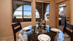 A dining area with a round glass table, four chairs, and a view of the beach through large windows. - Condo 24-1 El Dorado Ranch (San Felípe)