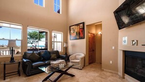 A spacious living room with a fireplace, large windows, a sofa, a coffee table, and a painting on the wall. - Condo 24-1 El Dorado Ranch (San Felípe)