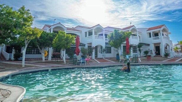 A swimming pool with a view of a white building with balconies and red umbrellas.