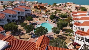 A resort with multiple buildings, a central swimming pool, and a view of the sea.