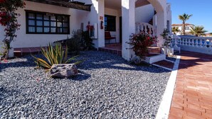 A white building with a balcony, a staircase, and a gravel pathway.