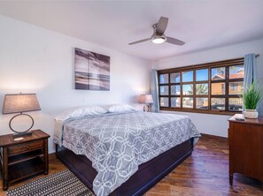 Relax in this serene bedroom with a large bed, ceiling fan, and a window offering a view of the outside.