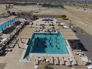 A swimming pool with lounge chairs and umbrellas, surrounded by a fenced area with a desert landscape in the background.