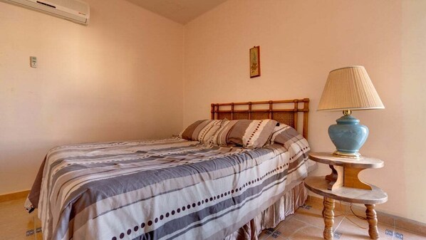 A bedroom with a bed, a bedside lamp, and a wall-mounted air conditioner.