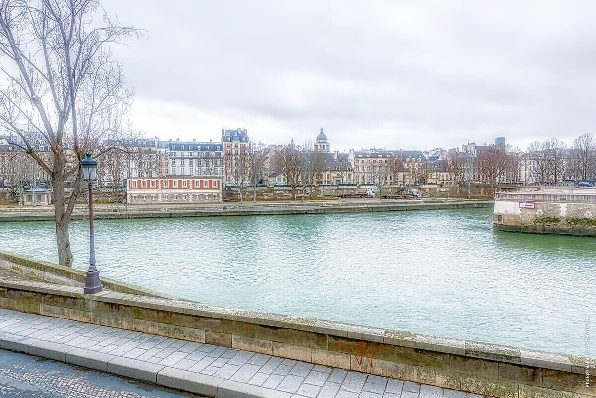 A riverside walkway with a view of historic buildings and a bridge.