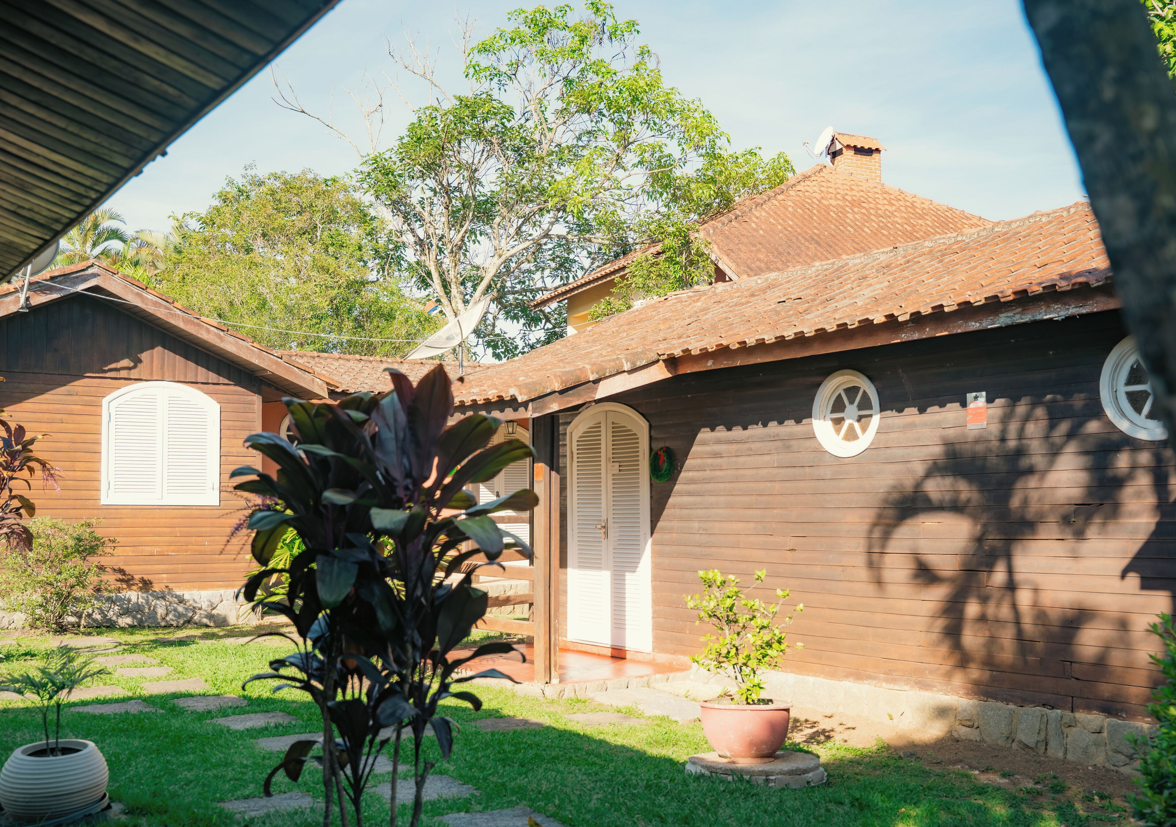 Una casa de madera con techo de tejas, un jardín con plantas en macetas y un cielo despejado.