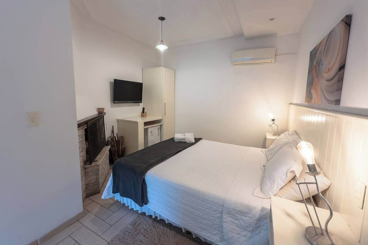 Een slaapkamer met een bed, nachtlamp, televisie, kledingkast en een open haard.