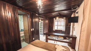 A room with a bed, a wooden ceiling, a TV mounted on the wall, and a window. - Pousada Flor De Penedo (Itatiaia)