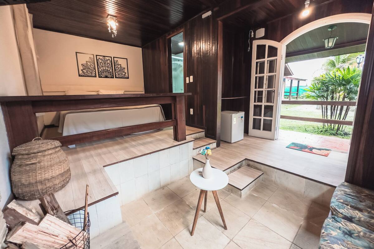 Een kamer met een bed, een klein tafeltje met een vaas, een gevlochten mand en uitzicht naar buiten.