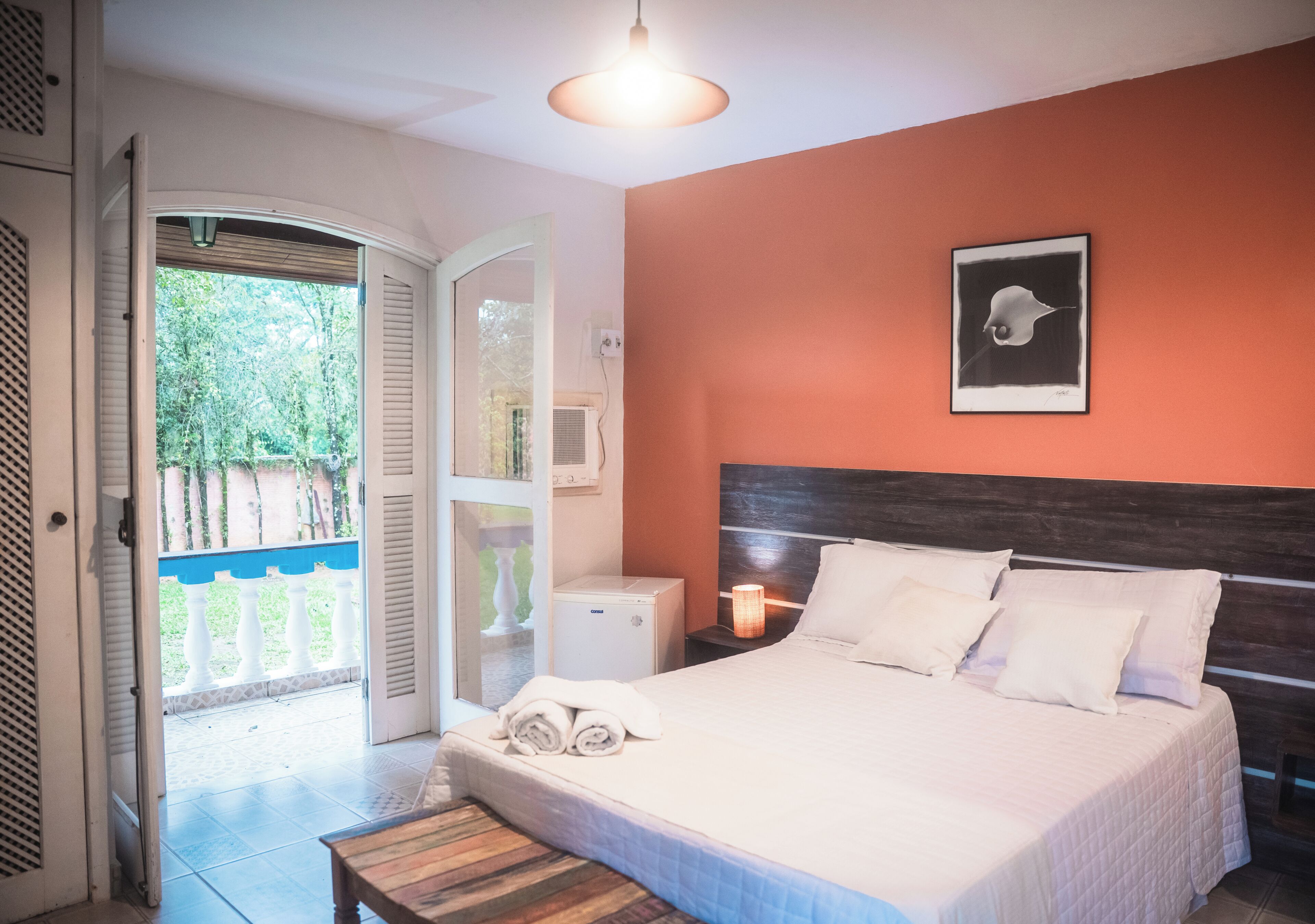 Een slaapkamer met een bed, nachtkastje, lamp en een foto aan de muur.