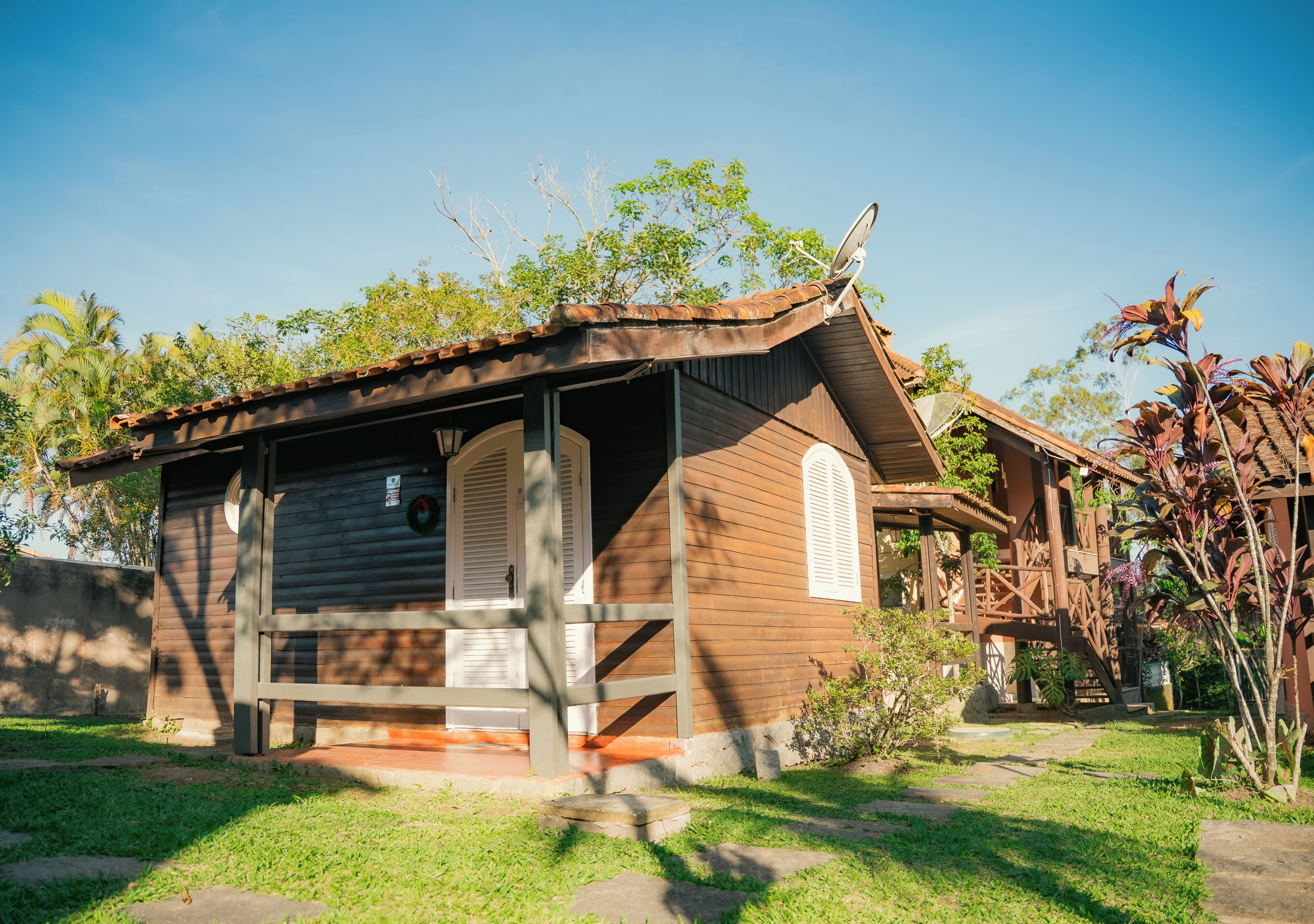 A wooden cabin with a porch, satellite dish, and a small garden area.