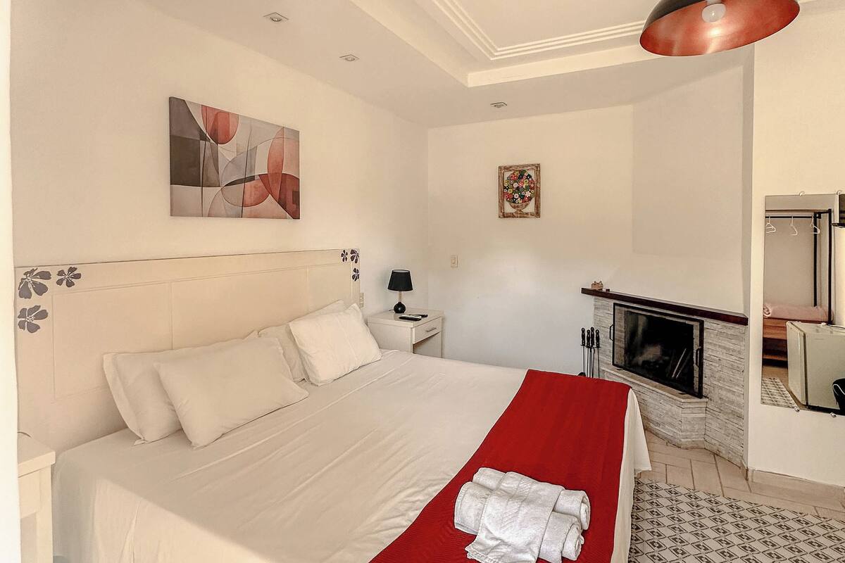 Een hotelkamer met een bed, een rode plaid, een open haard, een schilderij en een televisie.
