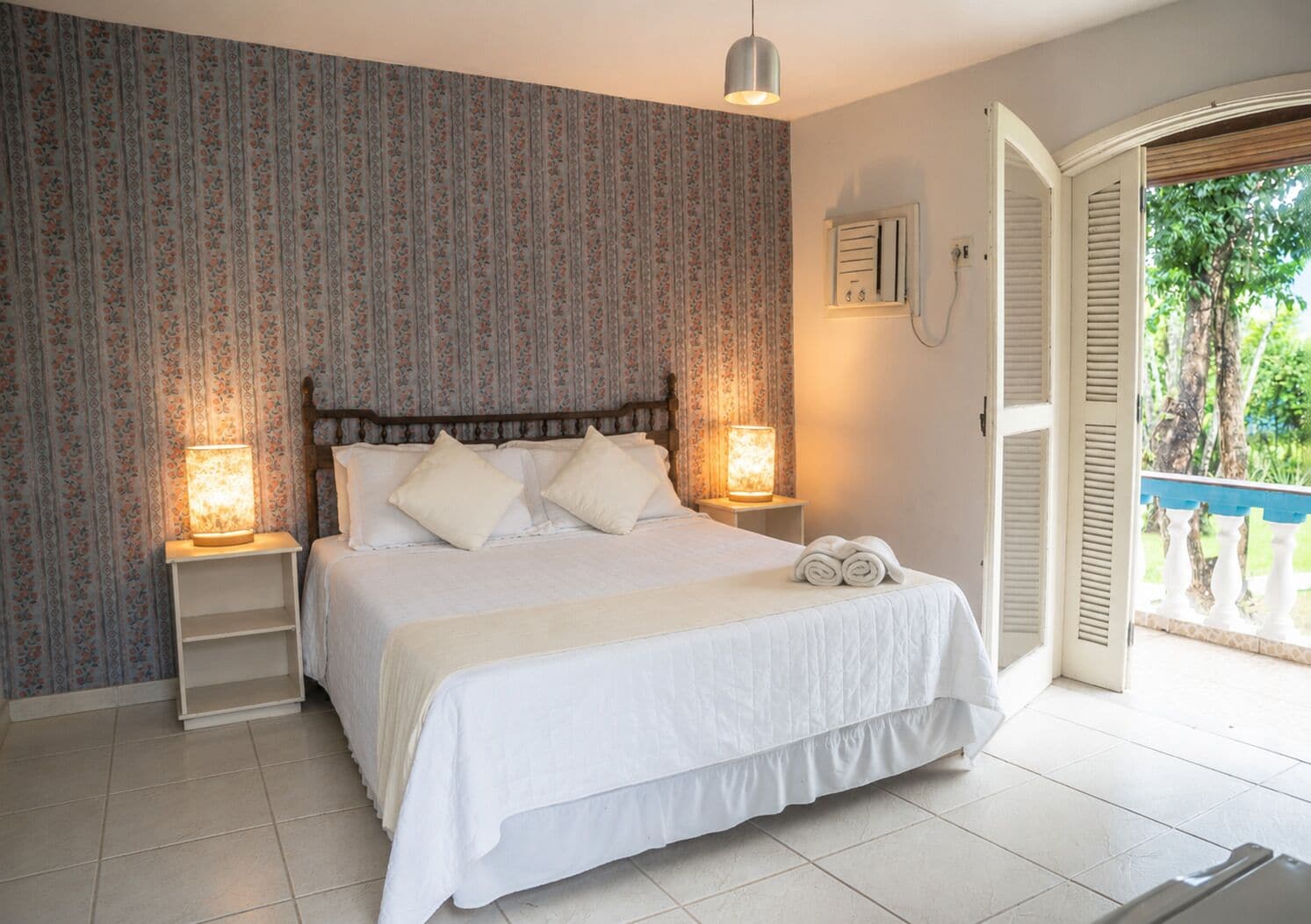 A bedroom with a bed, two bedside lamps, a window with a view, and a door leading outside.