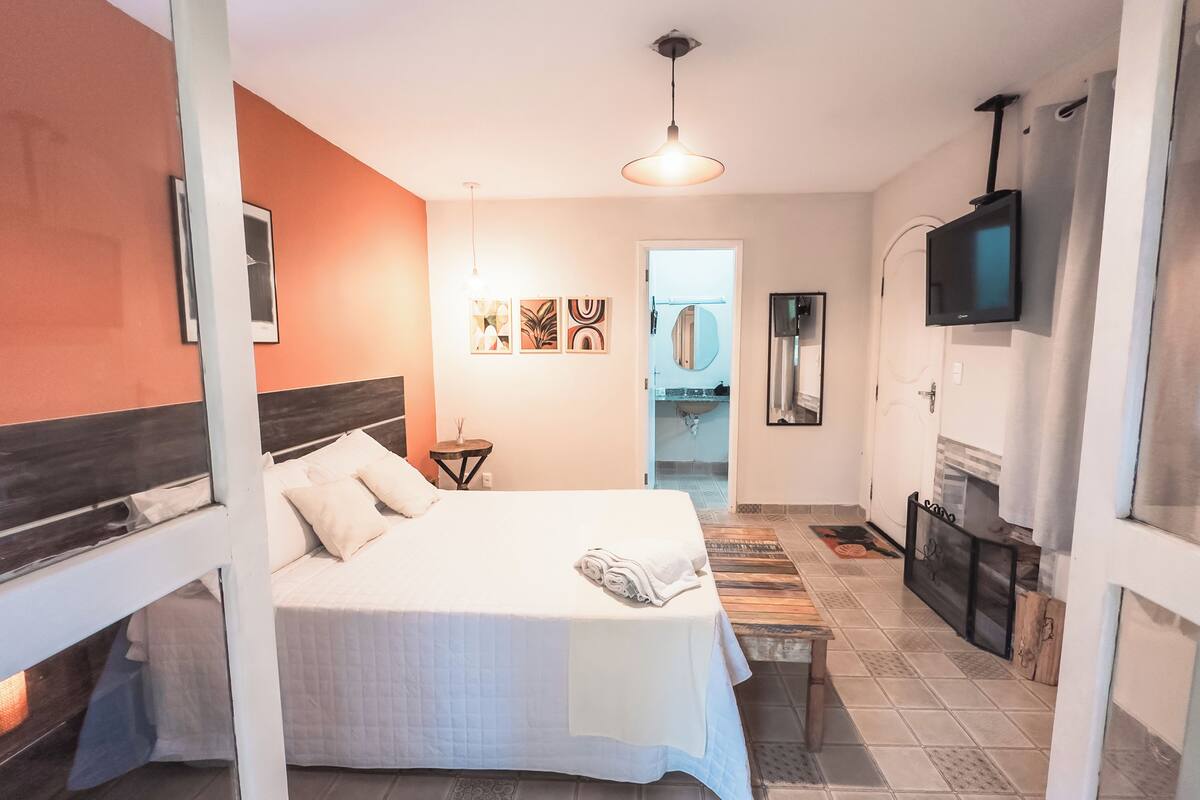 Een slaapkamer met een bed, een nachtkastje, een televisie en een zichtbare badkamer door een open deur.