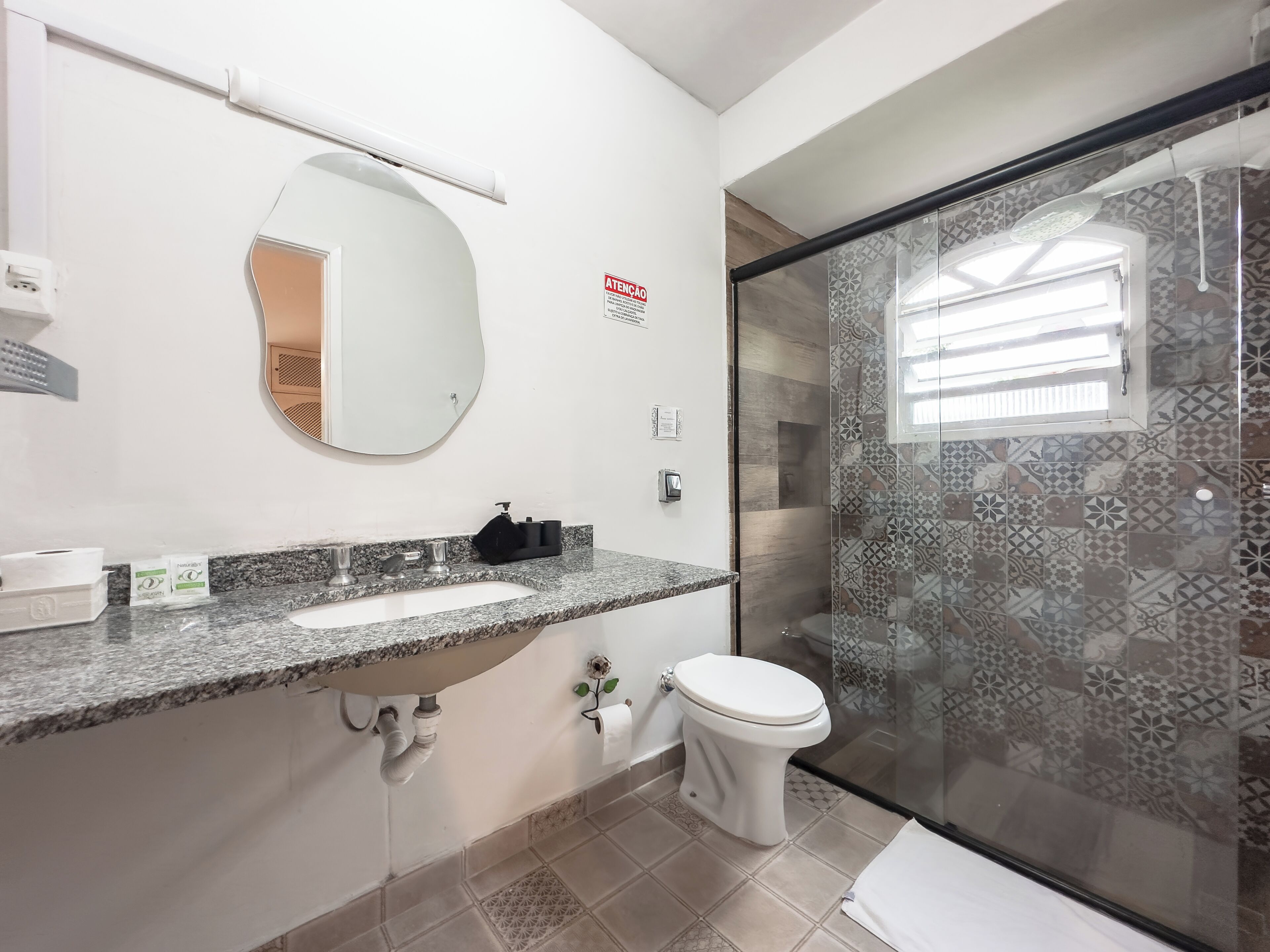 Uma casa de banho com bancada de granito, lavatório branco, sanita e chuveiro com azulejos estampados.