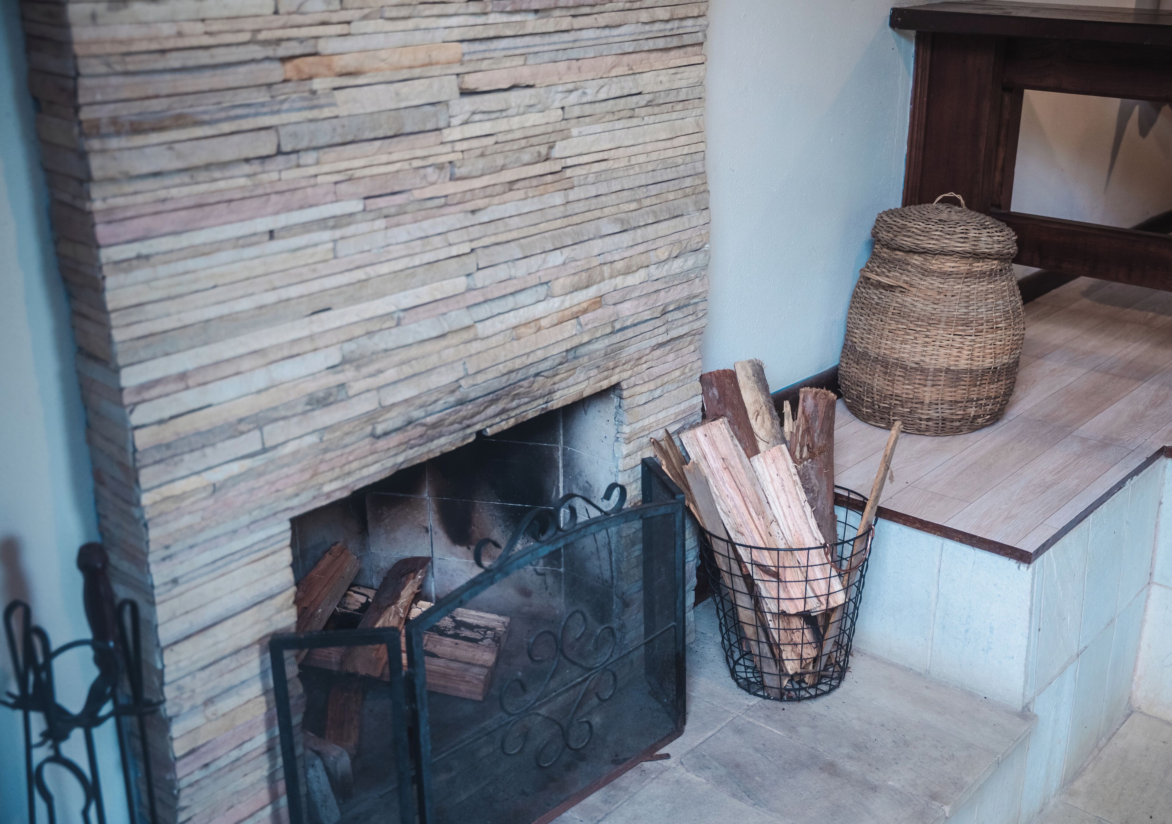 A fireplace with logs, a wicker basket, and a wooden table.