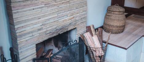 A fireplace with logs, a wicker basket, and a wooden table.