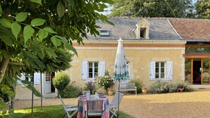 Un bâtiment rustique doté d’un patio avec jardin, d’une table dressée pour le repas et d’un banc.