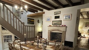 Un espace repas comprenant une table et des chaises en bois, une cheminée et un escalier menant à un niveau supérieur.