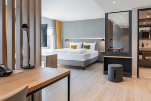 Una habitación de hotel moderna con cama, escritorio, lámpara y espejo.