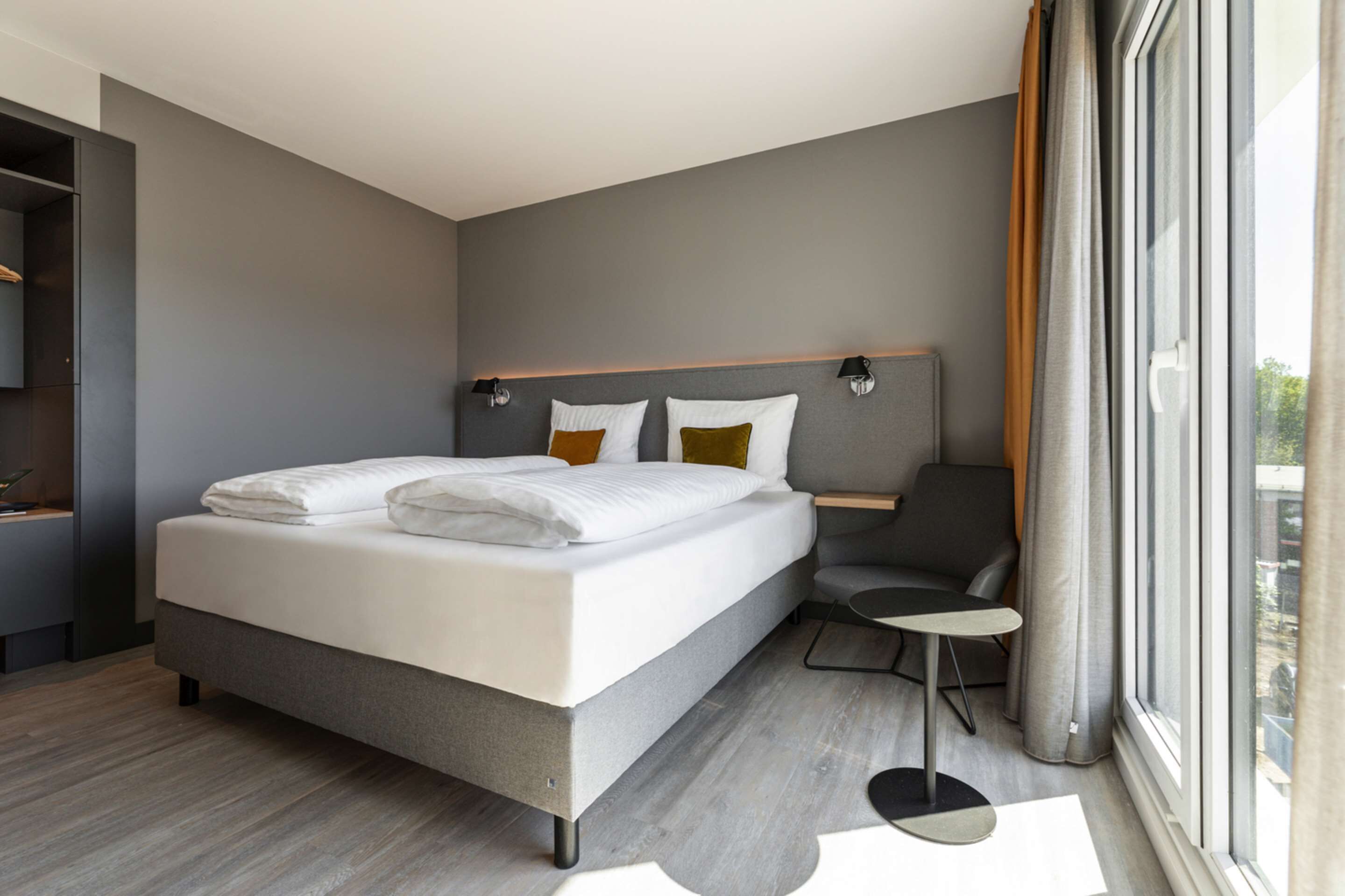Una habitación de hotel moderna con una cama grande, un escritorio pequeño y vistas al exterior a través de un ventanal amplio.