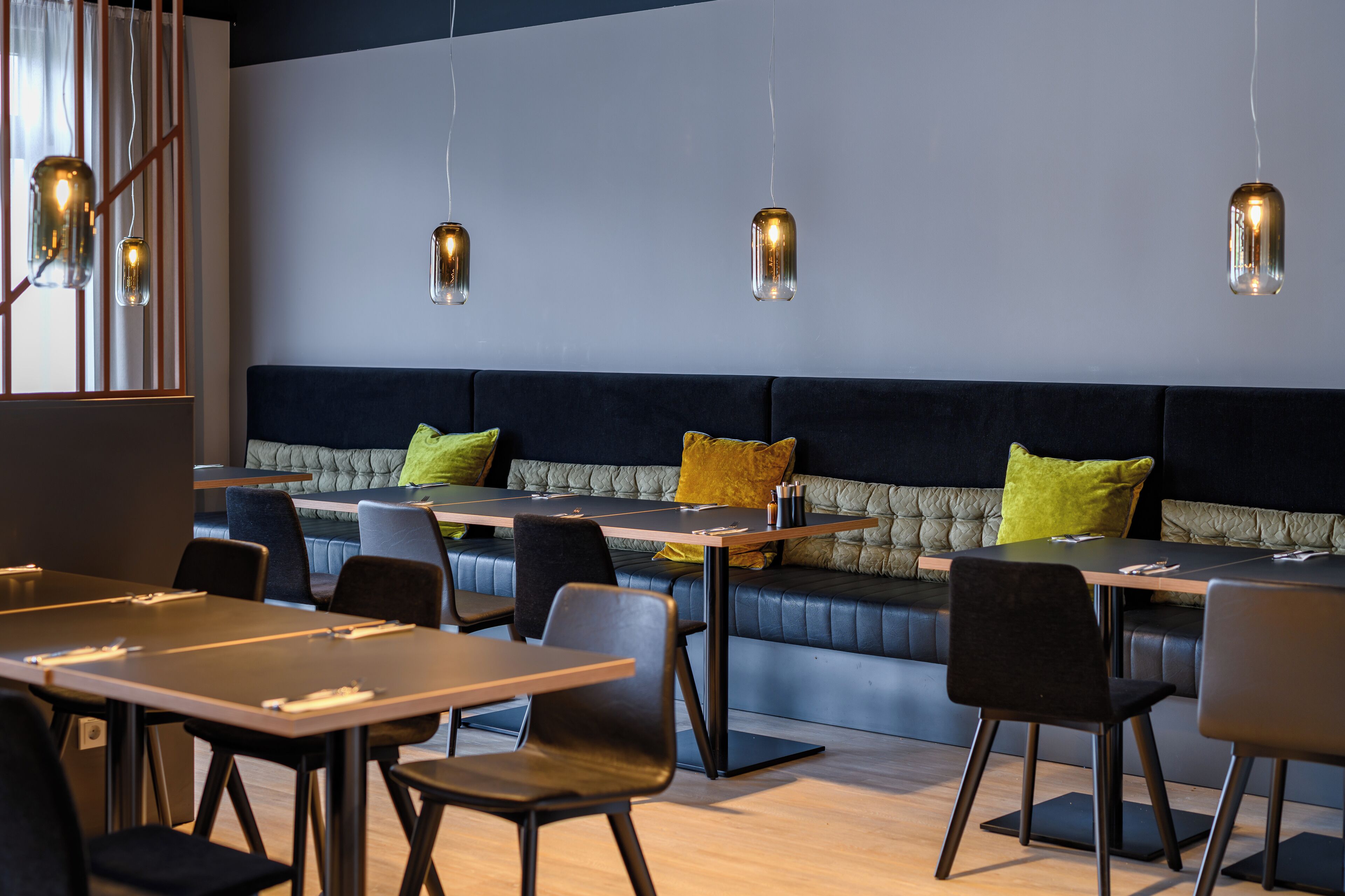 A modern dining area with tables and chairs, a cushioned bench, and pendant lighting.