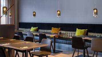 A modern dining area with tables and chairs, a cushioned bench, and pendant lighting.