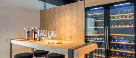 Zona de bar con mostrador de madera, taburetes negros y un enfriador de vinos con botellas.