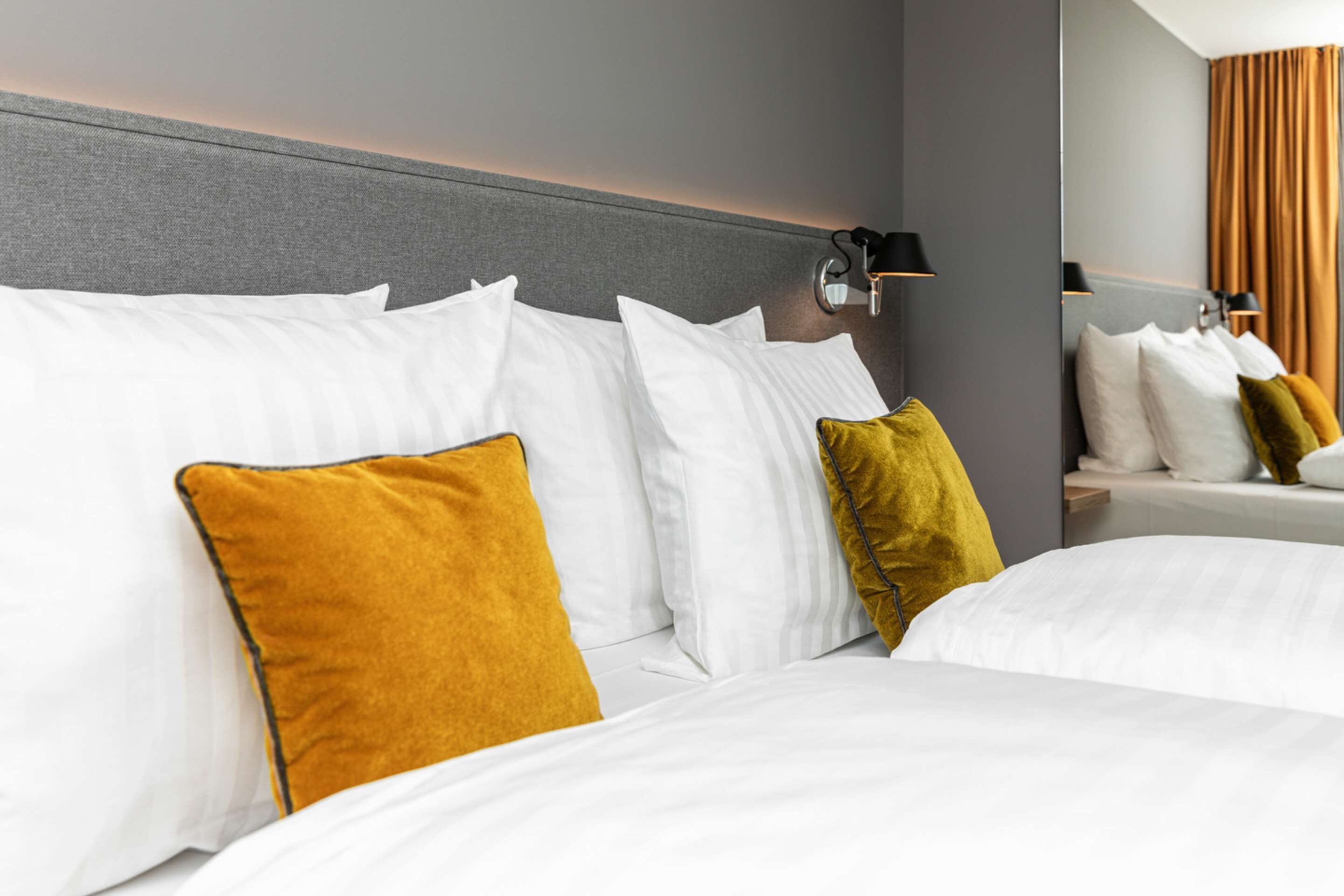 Habitación de hotel con una cama grande, varios almohadones, cabecera y una lámpara fijada a la pared.