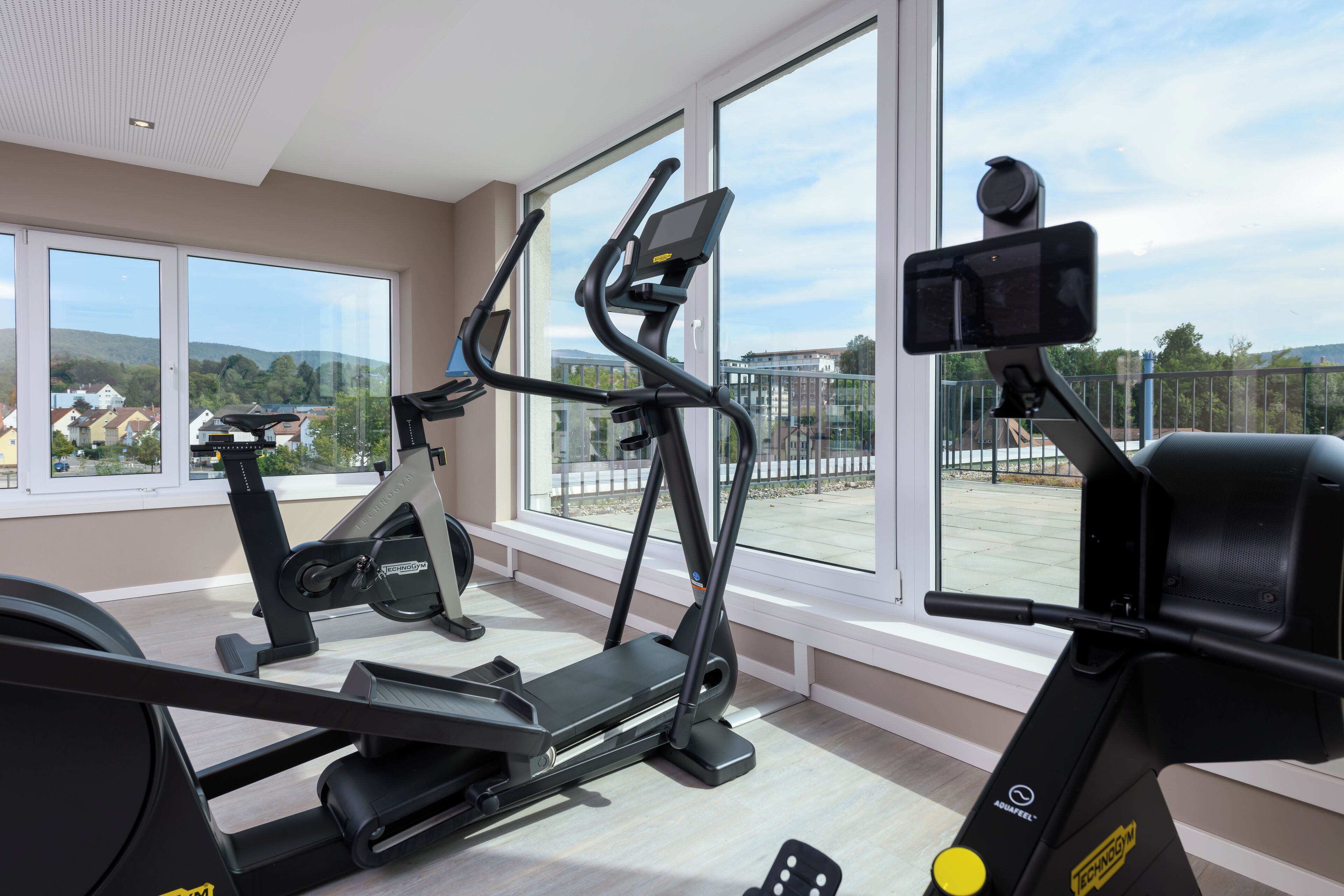 A home gym with exercise equipment, large windows, and a view of the neighborhood.