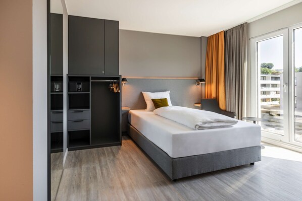Una habitación de hotel moderna con una cama grande, armario empotrado, mesitas de noche y un balcón con cortinas.