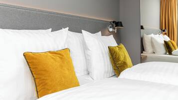 A hotel room with a neatly made bed, a headboard, and a wall-mounted lamp.