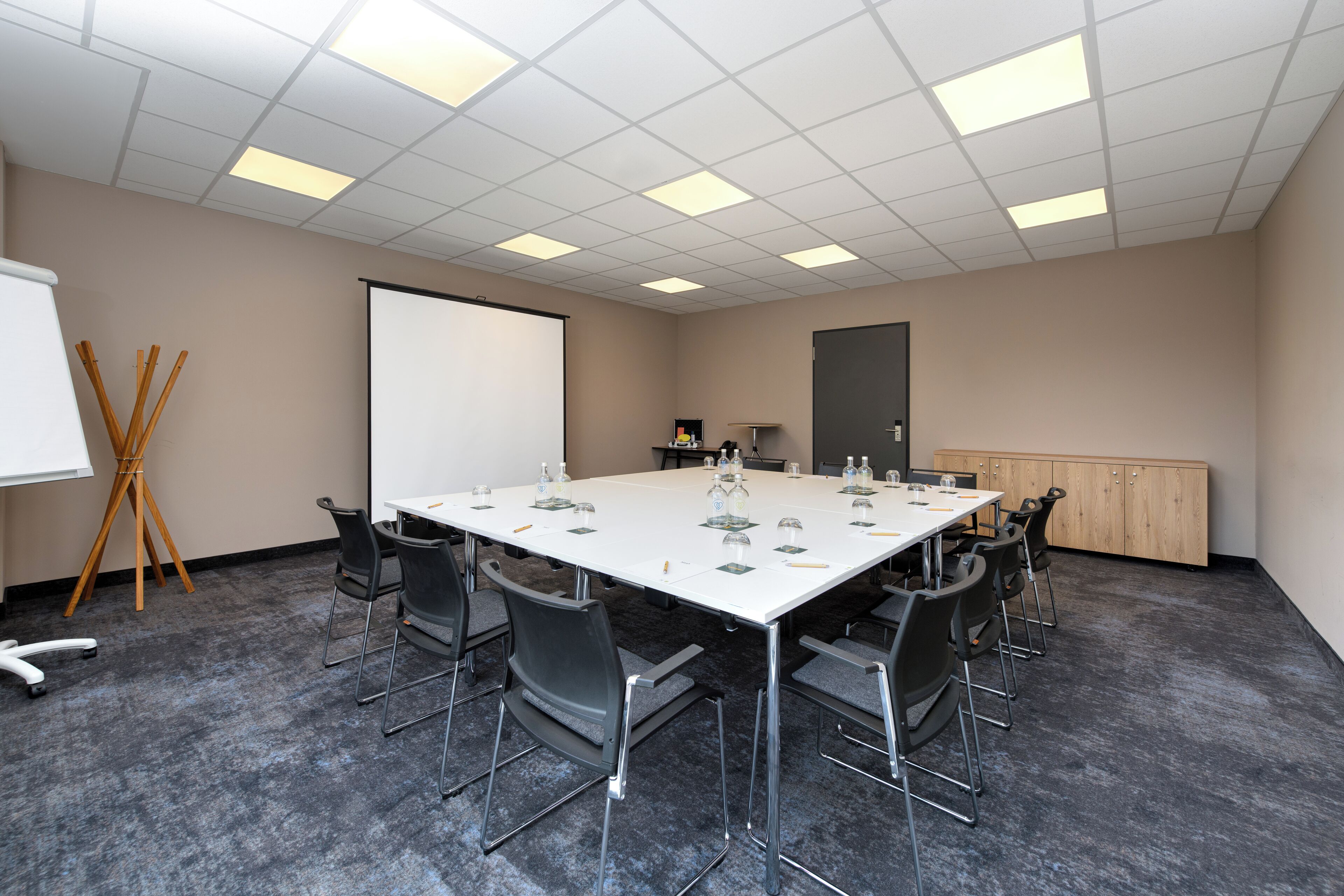 Un salón de conferencias con una gran mesa, sillas, una pantalla de proyector y una pizarra.