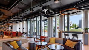 A modern hotel lobby with seating areas, a bar, and large windows offering views of the city. - Piazza Hotel und Restaurant (Aalen)