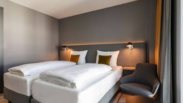 A modern hotel room with a double bed, two bedside tables, a chair, and a large window with curtains.