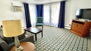 Camera d'albergo con tappeto a motivi, televisore, scrivania, sedia, lampada e cassettiera.