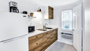 A modern kitchen with white cabinetry, wooden lower cabinets, a built-in microwave, and a coffee maker. - Ocean Breeze Motel - Kitchenette (South Yarmouth)