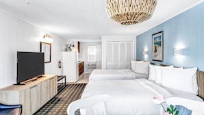 A hotel room with a bed, a desk, a television, a wardrobe, and a hanging light fixture. - Ocean Breeze Motel - Kitchenette (South Yarmouth)