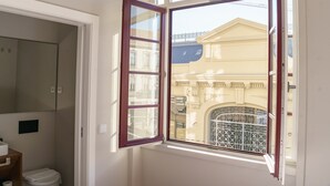 Quarto com uma janela grande, vista de um edifício com varanda e porta que dá para outro cômodo.