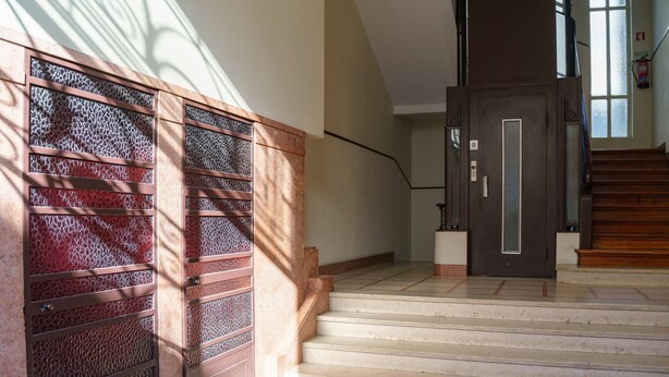 Uma escadaria com uma porta escura no topo, um corrimão e uma parede com textura.