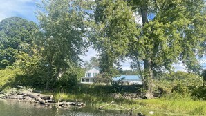 Una casa junto a un río tranquilo, rodeada de árboles frondosos y con un muelle.