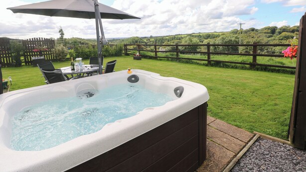 A hot tub with a table and chairs, surrounded by a wooden fence and a grassy lawn. - The Old Dairy (Clarbeston Road)