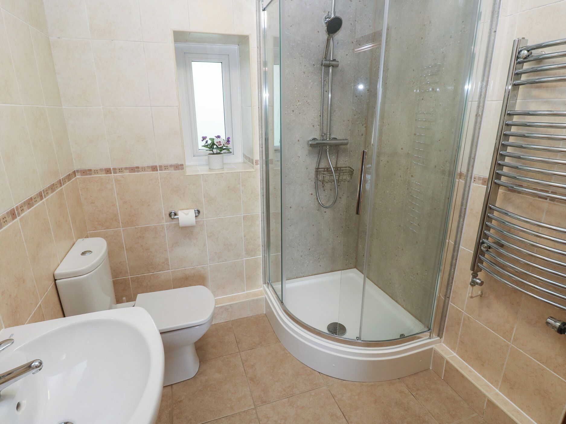 A bathroom with a toilet, sink, shower, and glass-enclosed shower stall.