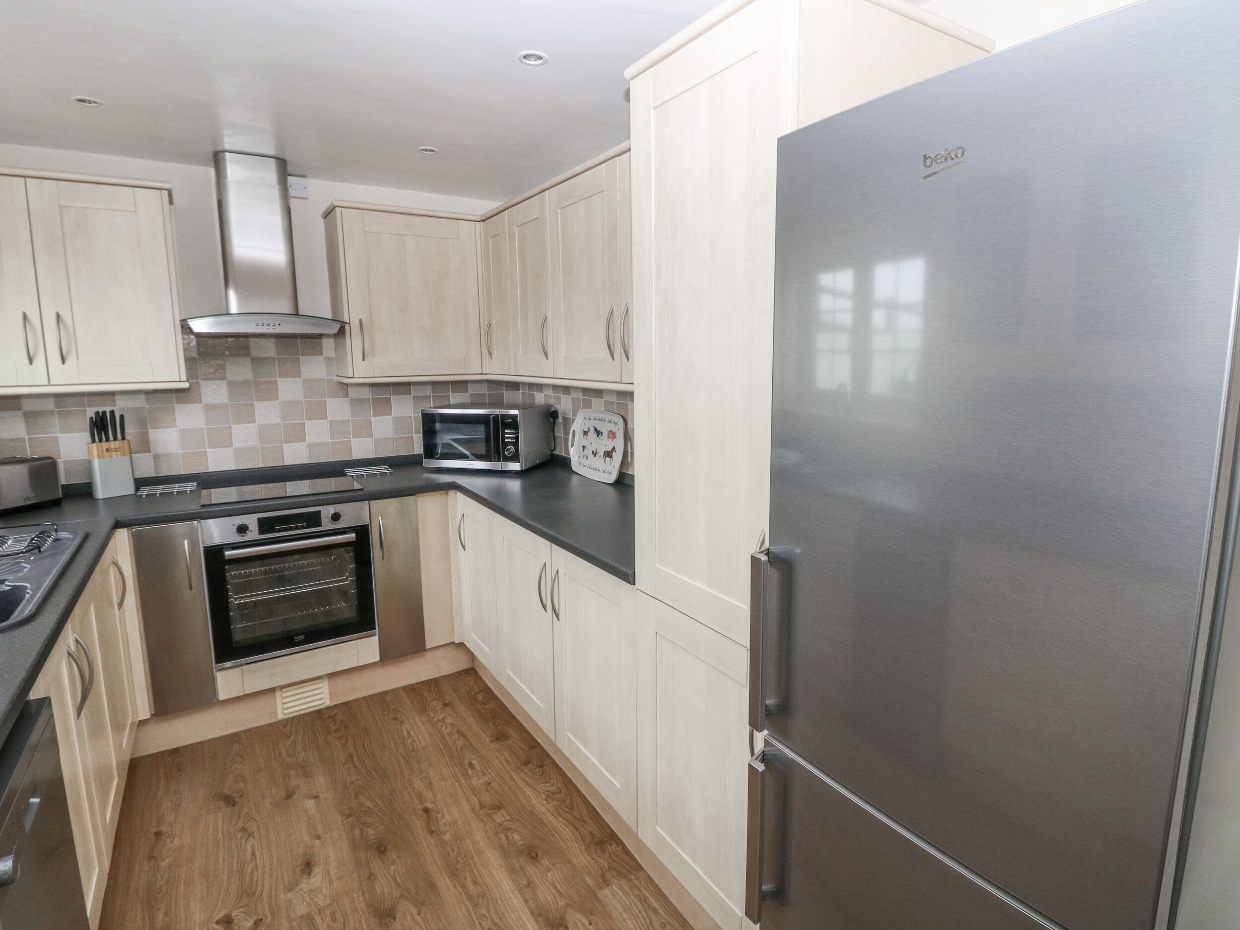 A modern kitchen with stainless steel appliances, light wood cabinetry, and a checkered tile backsplash.