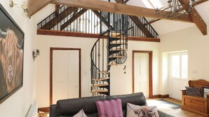 A spacious living room with a black leather sofa, a wooden staircase, and a large painting on the wall. - The Old Dairy (Clarbeston Road)