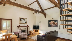A spacious living room with wooden beams, a fireplace, a television, a sofa, and a spiral staircase. - The Old Dairy (Clarbeston Road)