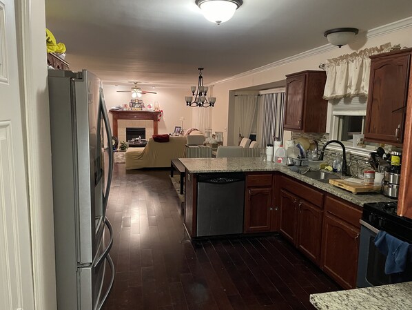 Kitchen with central island, sink, and dishwasher, adjacent to a cozy dining area with a sofa and fireplace.