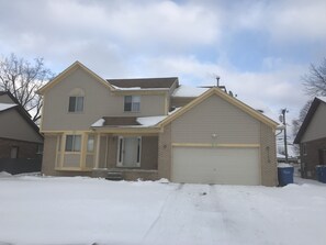 Enter through the central entrance, featuring a covered porch and garage with a white door, set against a brick facade.