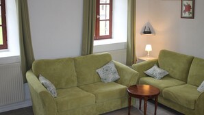 A living room with two green sofas, a small wooden table, a lamp, and a window with curtains.