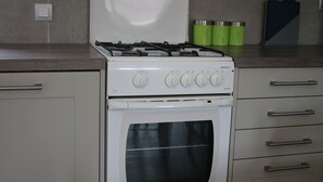 A kitchen with a white stove, oven, and stainless steel handles. There are green containers on the counter and a knife block with knives.